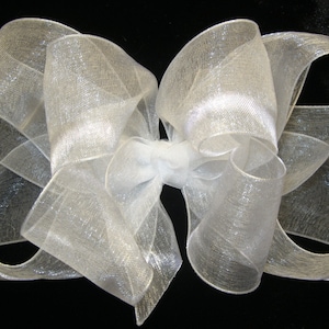 May include: A large white sheer bow with a shimmery finish. The bow is made of multiple layers of fabric and is tied in a classic bow shape.