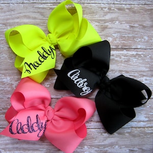 May include: Three large hair bows in different colors. The bows are made of grosgrain ribbon and are personalized with names. The bows are yellow, black, and pink.