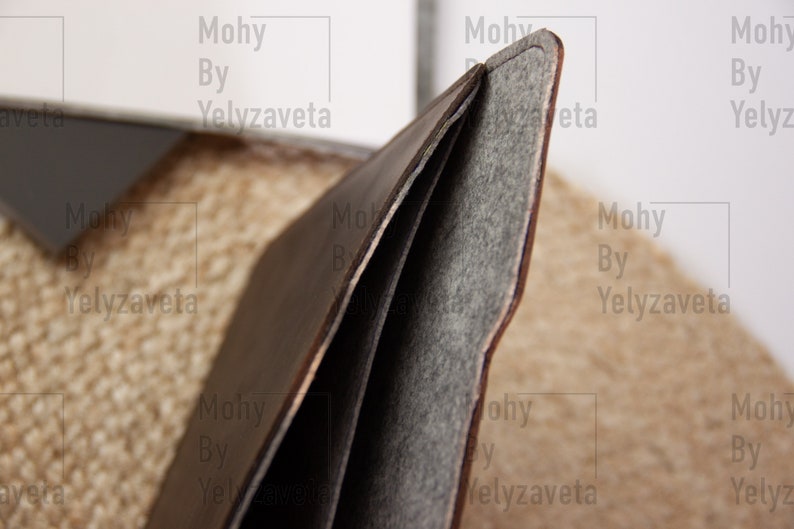 May include: A brown leather laptop sleeve with a gray felt lining. The sleeve is folded open to show the lining.