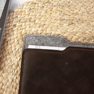 May include: A brown leather folder with a gray felt lining. The folder is closed and has a white piece of paper inside.