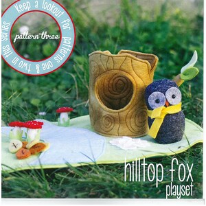 May include: A felt playset with a tree trunk house and an owl wearing a yellow scarf. The text "MAY blossom designs by Simone Gooding" and "hilltop fox playset" are visible. The image also includes felt mushrooms and other decorative elements.