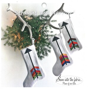 May include: Three white Christmas stockings with black arrow designs and colorful patchwork fabric accents. The stockings are hanging on a white antler with a green garland and white lights. The text "Straight and Narrow" is at the top of the image. The text "Sewn into the fabric... Pieces of our lives" is at the bottom of the image.