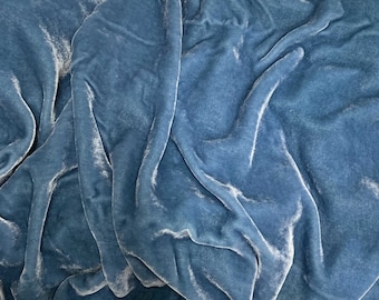 May include: Close-up of a soft, blue velvet fabric with a smooth, silky texture. The fabric is draped and folded, creating a luxurious and elegant look.