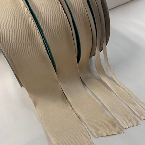 May include: A set of beige grosgrain ribbon spools in various widths. The ribbon is a woven fabric with a subtle texture.