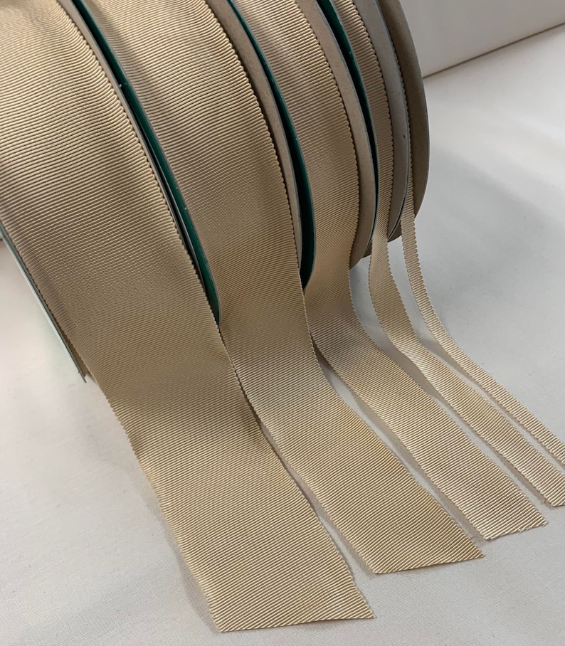May include: A set of beige grosgrain ribbon spools in various widths. The ribbon is a woven fabric with a subtle texture.