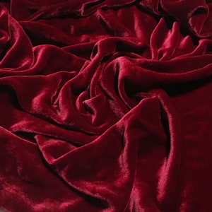 May include: A close-up shot of a deep burgundy velvet fabric. The fabric is draped and folded, creating shadows and highlights that emphasize its soft texture. The rich color and luxurious appearance suggest a high-quality textile.
