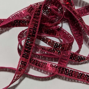 May include: A close-up of a spool of red sequined trim. The trim is made of a thin, red fabric with a row of small, shiny sequins.