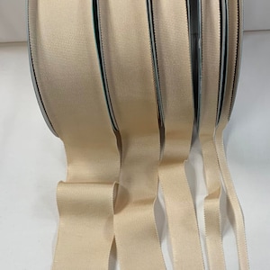 May include: Four spools of beige grosgrain ribbon in different widths. The ribbon is a smooth, woven fabric with a subtle sheen.