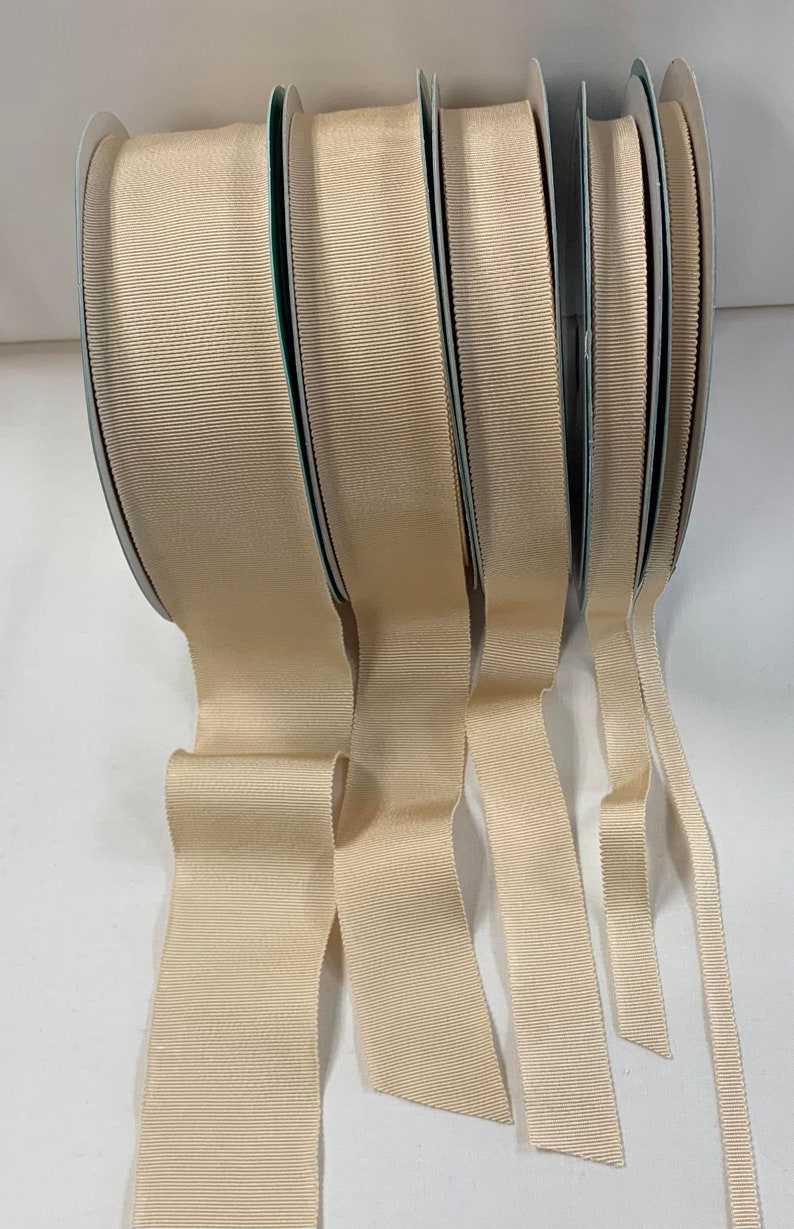 May include: Four spools of beige grosgrain ribbon in different widths. The ribbon is a smooth, woven fabric with a subtle sheen.