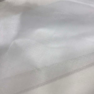 May include: A sheer white fabric with a delicate, semi-transparent quality and a subtle, fine-grained texture. The material is draped in soft, flowing folds, creating light and shadow across the surface, highlighting its lightweight and airy nature.
