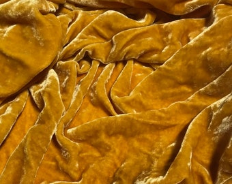 Könnte beinhalten: Nahaufnahme eines weichen, goldgelben Samtstoffes. Der Stoff ist drapiert und gefaltet und erzeugt so einen luxuriösen und strukturierten Look.
