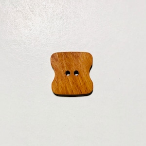 May include: A wooden button with two holes in the shape of a rectangle with rounded corners.