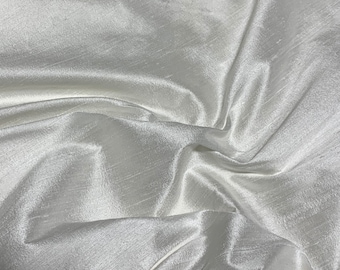 May include: White silk fabric with a smooth, lustrous finish. The fabric is draped and folded, showcasing its soft texture and subtle sheen.