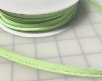 Puede incluir: Una bobina de cinta de bies de color verde claro con un núcleo blanco. La cinta está doblada y cosida a lo largo del borde.