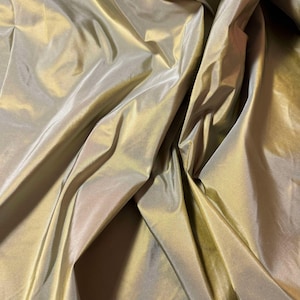 May include: A close-up of a smooth, iridescent fabric with a subtle sheen. The fabric is a light gold color with a hint of green.