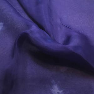 May include: A piece of sheer, purple fabric with a soft, flowing texture. The fabric is draped and folded, creating a sense of movement and depth.