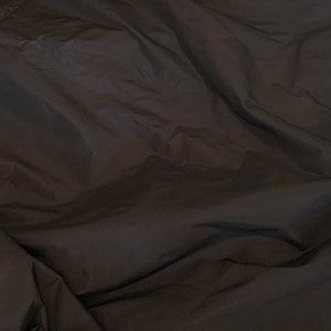 May include: A close-up of a dark brown fabric with a smooth, silky texture. The fabric is folded and draped, creating soft, flowing lines.