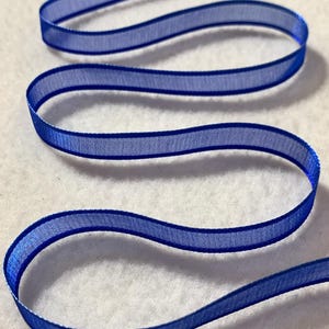 May include: A roll of royal blue sheer ribbon with a satin edge. The ribbon is approximately 1/4 inch wide.