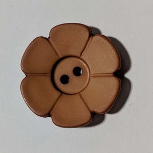 May include: A brown flower-shaped button with six petals and two black holes in the centre. The button is made of a smooth material and is designed to be sewn onto clothing or other fabric items.