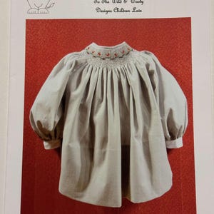 May include: A light grey baby dress with a smocked neckline and puffed sleeves. The dress has a rounded hem and white cuffs. The text "Pat Garretson Designs" and "324 Winter" are visible.