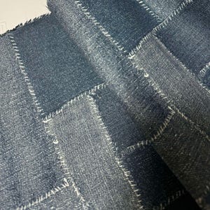Könnte beinhalten: Nahaufnahme eines blauen Jeansstoffes mit Patchwork-Muster. Der Stoff besteht aus verschiedenen Teilen aus Jeans, die mit weißem Garn zusammengenäht sind.