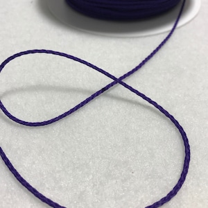 May include: A close-up of a spool of purple cord. The cord is wound tightly around the spool and is ready to be used for crafting or other projects.