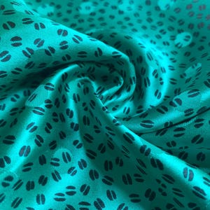 May include: A vibrant emerald green fabric featuring a repeating pattern of small, dark, oval-shaped marks. The material has a smooth, satin-like sheen and is gathered into soft, flowing folds that create depth and texture across the surface.