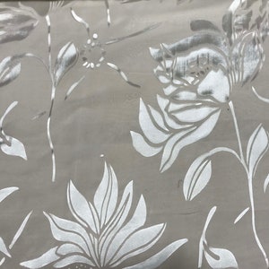Puede incluir: Tela floral blanca con un brillo metálico plateado. La tela presenta un patrón repetitivo de flores y hojas estilizadas.