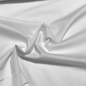 May include: White fabric with a smooth, silky texture. The fabric is folded and draped, showcasing its soft and flowing nature.