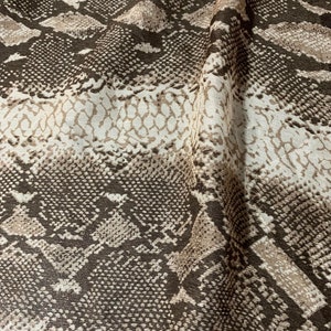Può includere: Tessuto con motivo a pelle di serpente marrone e bianco con una superficie testurizzata.