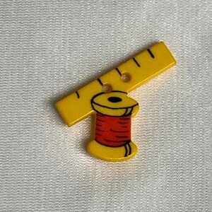 May include: Yellow plastic button with a red and yellow spool of thread and a yellow ruler with black markings.