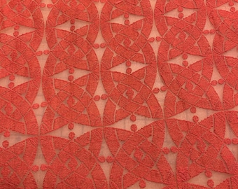 May include: Red fabric with a repeating geometric pattern of overlapping circles and triangles. The fabric has a subtle sheen and a textured surface.