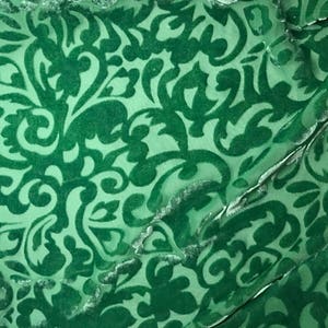 Puede incluir: Tela de terciopelo verde con un patrón de damasco. La tela tiene un diseño en relieve texturizado.