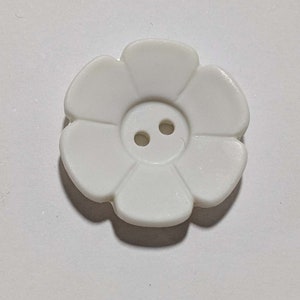 May include: White plastic flower-shaped button with two holes.