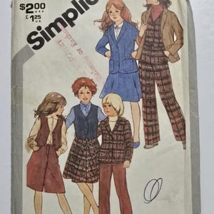 Peut inclure: Patron de couture Simplicity vintage pour vêtements de filles. La couverture présente des illustrations d'enfants dans diverses tenues, dont un blazer et une jupe bleus, un tailleur pantalon à carreaux et un ensemble short. Le prix du patron est de 2,00 $.