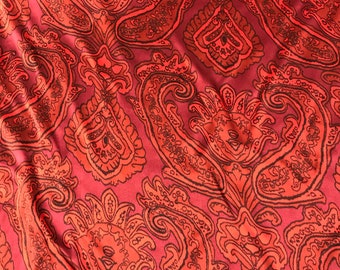 May include: Red fabric with a paisley pattern in black and orange. The fabric has a soft, silky texture.