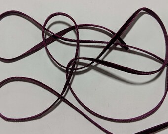 May include: A length of dark burgundy velvet ribbon, twisted and looped on a white background.