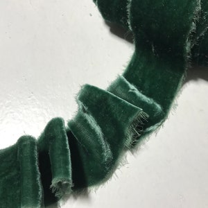 May include: A close-up of a green velvet ribbon with frayed edges. The ribbon is folded and ruffled, creating a soft and textured look.