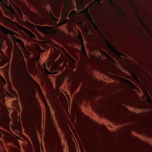 Puede incluir: Primer plano de una tela de terciopelo rojo oscuro con una textura suave y lujosa. La tela está drapeada y doblada, creando un aspecto dramático y elegante.
