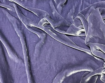 May include: A close-up of a soft, smooth, purple velvet fabric. The fabric is draped and folded, showing its texture and sheen.