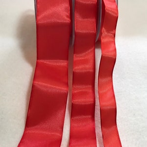 May include: Three spools of bright red satin ribbon. The ribbon is unwound from the spools, showing the shiny, smooth texture. The ribbon is a solid, vibrant red color, perfect for crafts and gift wrapping.