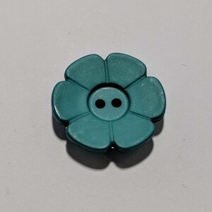 May include: A teal blue flower-shaped button with two holes in the center.