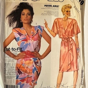 以下が含まれることがあります： ヴィンテージMcCall'sの縫製パターン。2つのドレスのデザインが含まれています。ラップドレスとVネックのドレスのパターンです。「Easy McCall's」と「Cut-to-Fit」のテキストが書かれたドレスのイラストが表紙に描かれています。