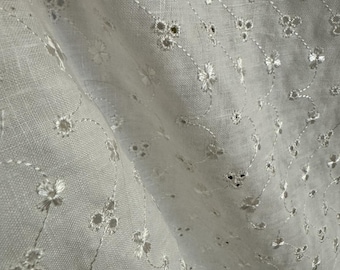May include: White cotton fabric with a delicate floral embroidery pattern. The fabric is sheer and lightweight, with a soft, drapey texture.