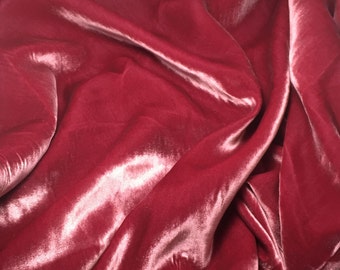 May include: Close-up of a deep red velvet fabric with a smooth, silky texture. The fabric is draped and folded, creating soft, flowing lines.