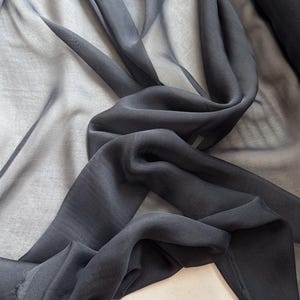 May include: Black sheer fabric with a soft, flowing texture. The fabric is draped and folded, showcasing its transparency and drape.
