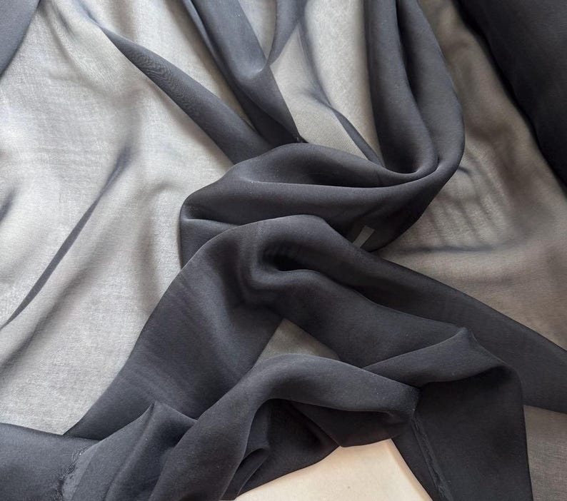 May include: Black sheer fabric with a soft, flowing texture. The fabric is draped and folded, showcasing its transparency and drape.