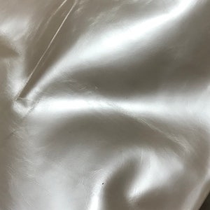 May include: Close-up of a smooth, white, faux leather fabric. The fabric has a subtle sheen and a slightly textured surface.