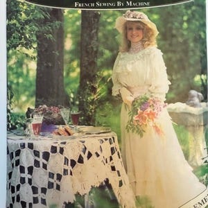 Puede incluir: Portada de libro con el título "Heirloom Sewing for Women" y el subtítulo "French Sewing By Machine". La imagen presenta a una mujer con vestido y sombrero blancos, sosteniendo flores. Una mesa con un mantel de encaje blanco en primer plano.
