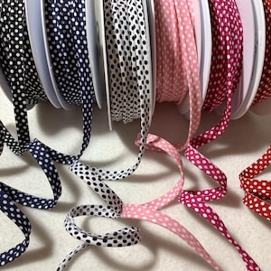 Op de afbeelding: Spoelen met wit lint van stof met zwarte, donkerblauwe, roze en rode stippen.